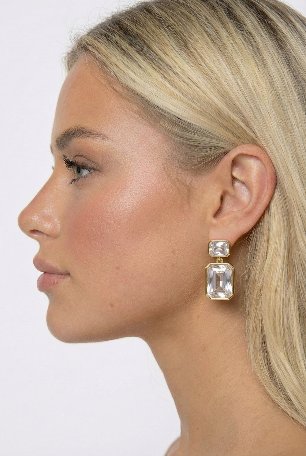 Close-up of a woman wearing clear gemstone earrings against a plain background