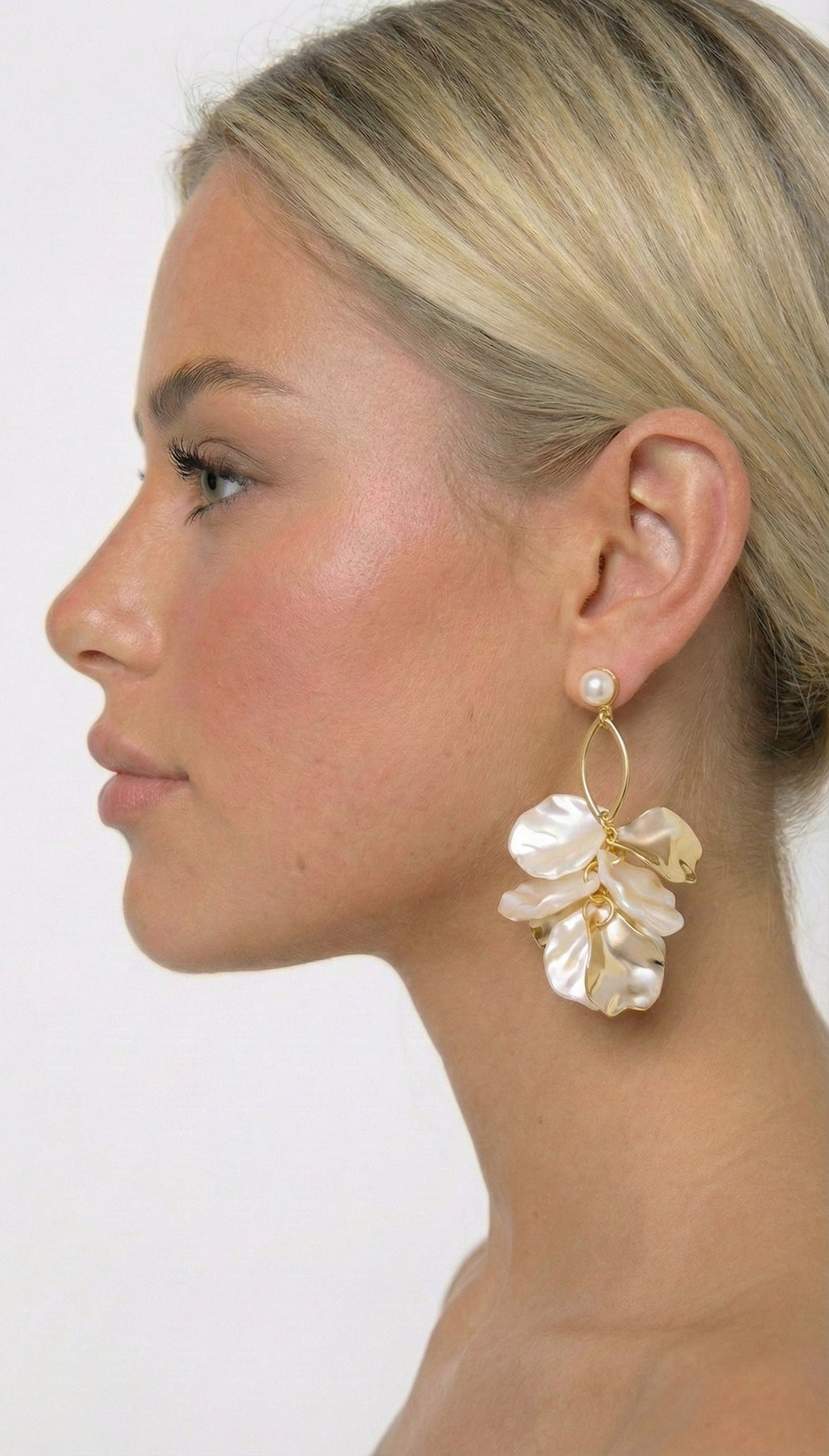 Woman wearing a floral earring with a gold and pearl design on a plain background