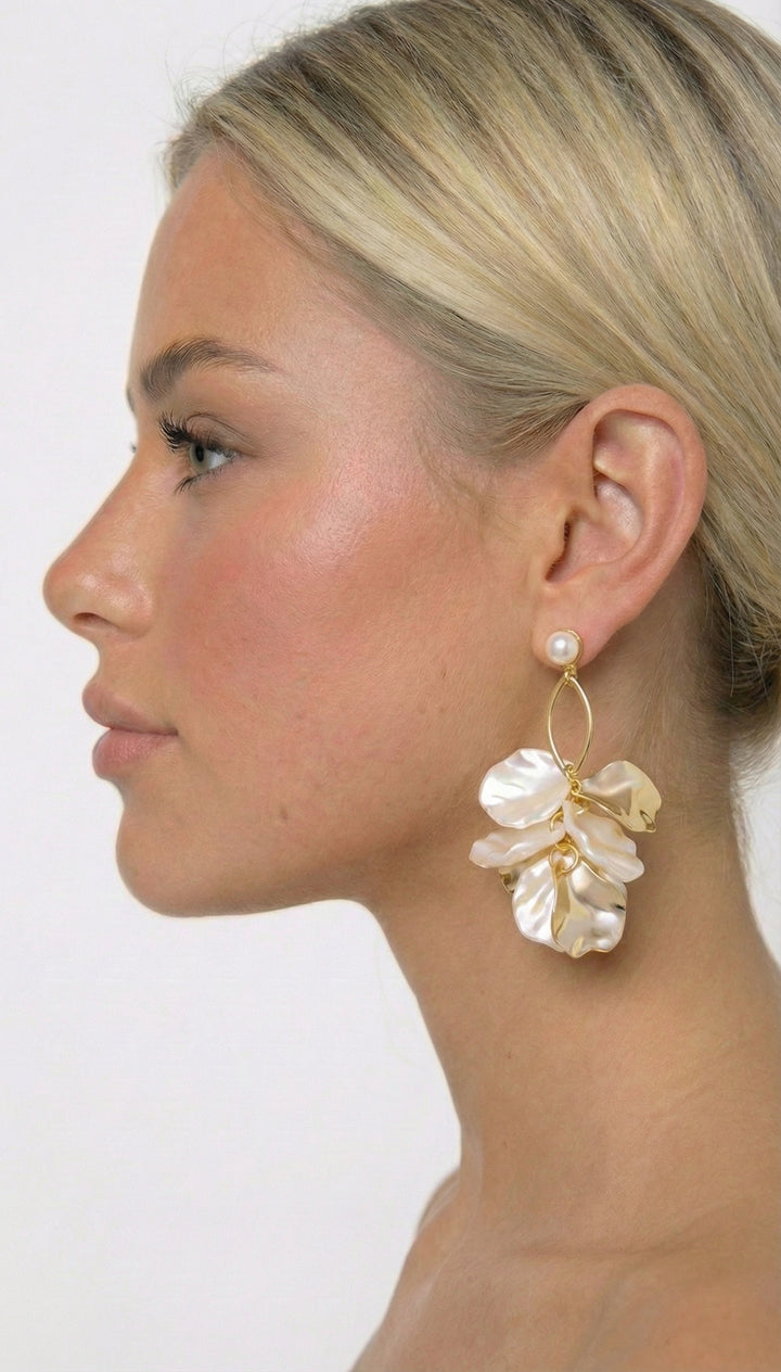 Woman wearing a floral earring with a gold and pearl design on a plain background