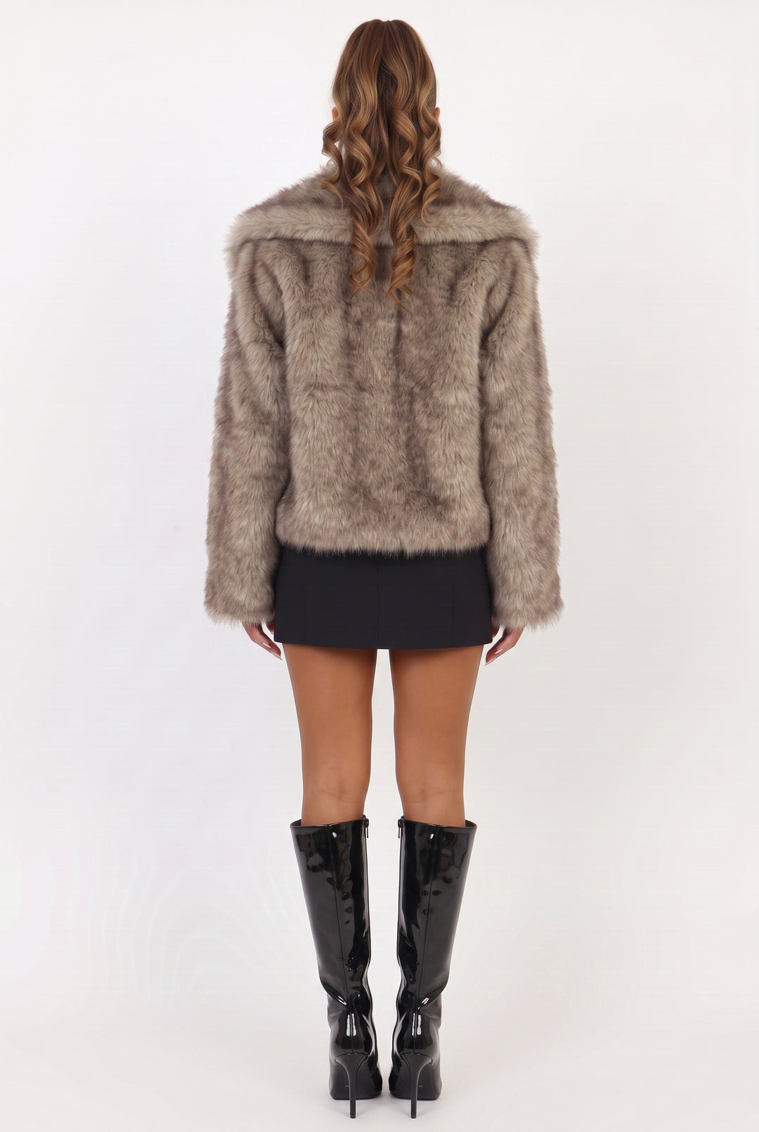 A woman shown from the back wearing a shaggy taupe faux fur jacket, a black mini skirt, and black patent leather knee-high boots against a white studio background.