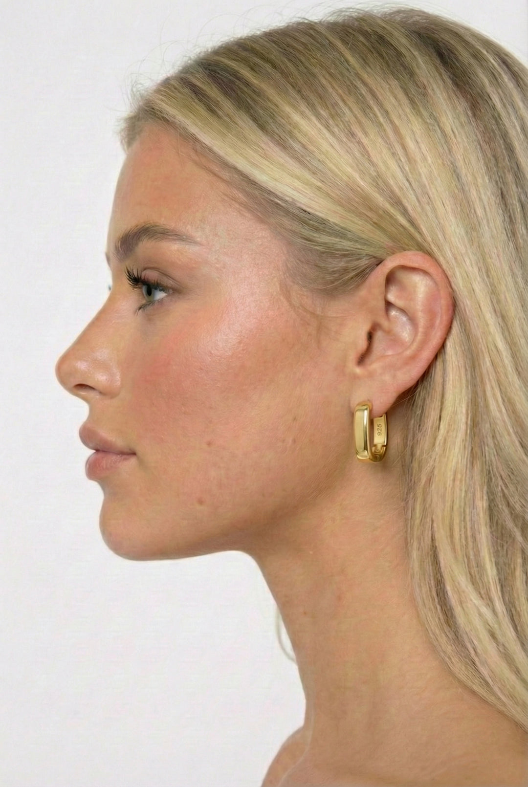 Close-up of a woman wearing gold hoop earrings against a white background