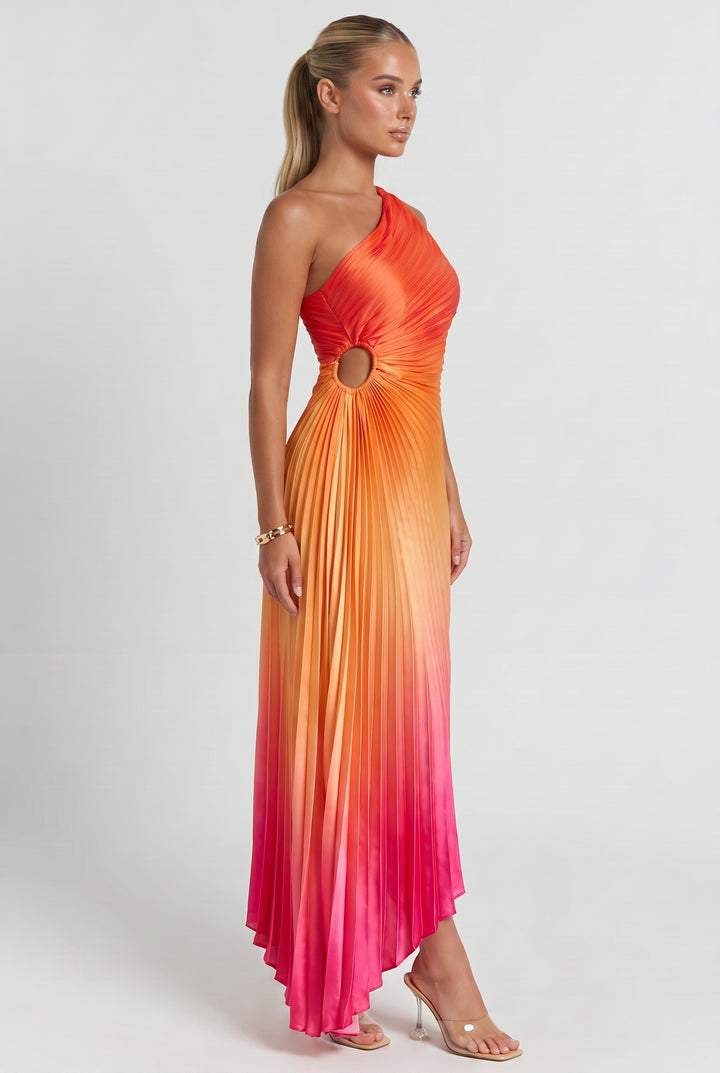 A woman modeling a one-shoulder pleated maxi dress with a gradient color story transitioning from bright orange at the bodice to yellow and pink at the skirt, featuring a circular cutout at the waist.