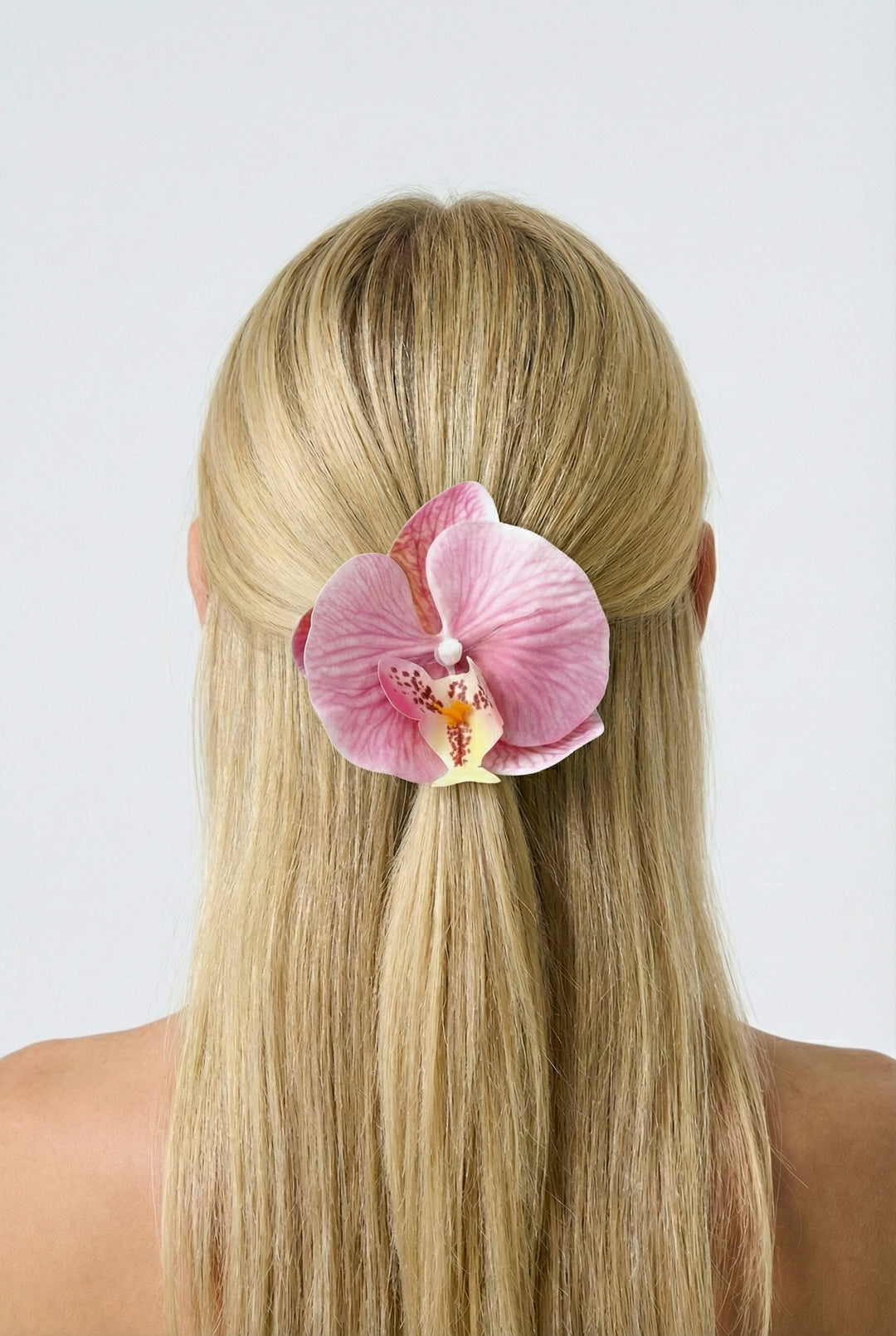 Person with pink orchid hair clip in blonde hair against a white background